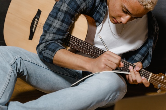 Musician songwriting on guitar or another instrument to overcome songwriter's block