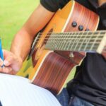 Musician with guitar, pen, and notebook for How To Write A Song With Great Lyrics article