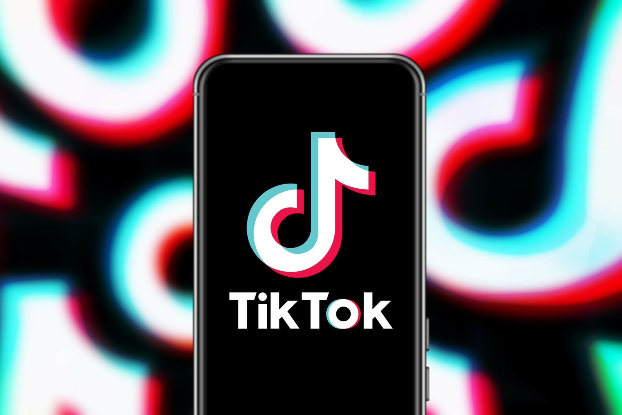 Mobile phone displaying the TikTok logo against a background made up of a mashup of TikTok logos for the article: Creating TikTok Ads For Bands And MusiciansCreating TikTok Ads For Bands And Musicians