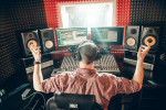 Musician sitting behind PC screens, monitors and mixing tables in a recording studio